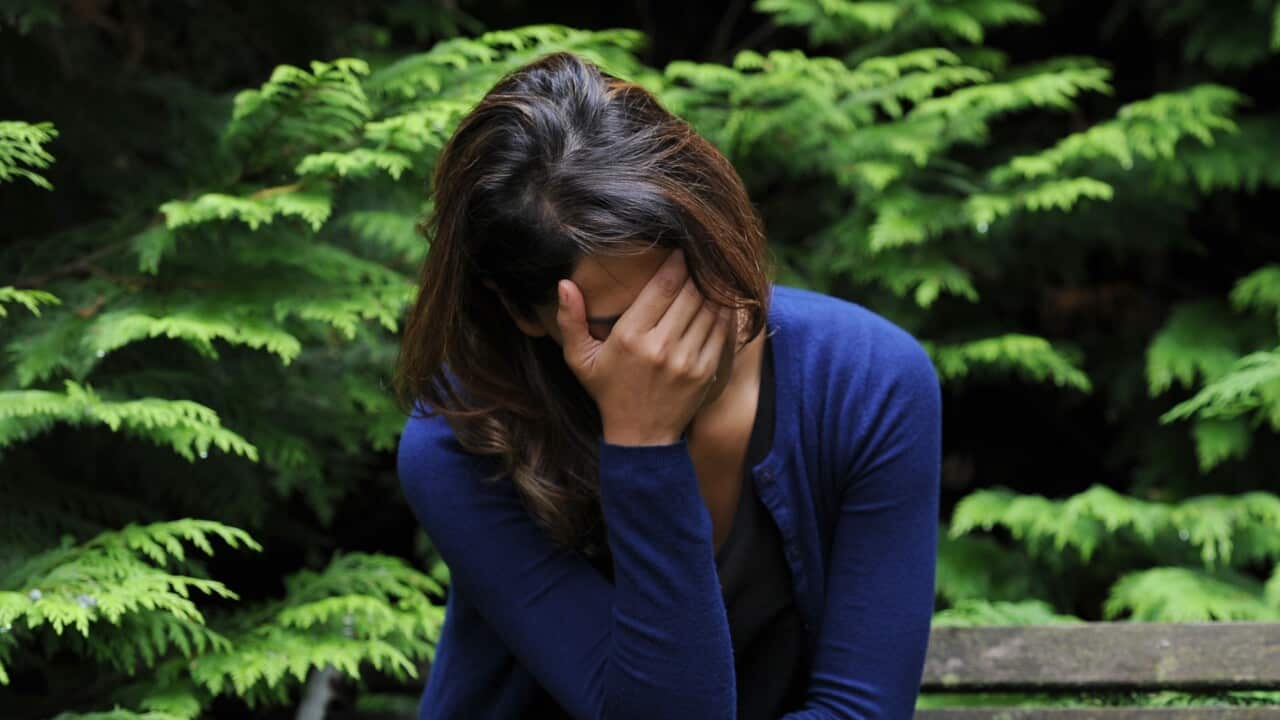 A woman sitting on a bench in a park with her head in her hand