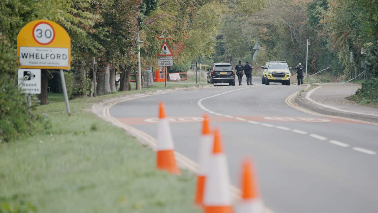 Road lined with traffic cones and a 30 km/h speed limit sign at the entrance to Whelford, with police vehicles and officers visible in the distance.