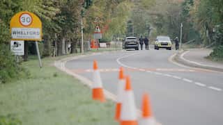 Road lined with traffic cones and a 30 km/h speed limit sign at the entrance to Whelford, with police vehicles and officers visible in the distance.