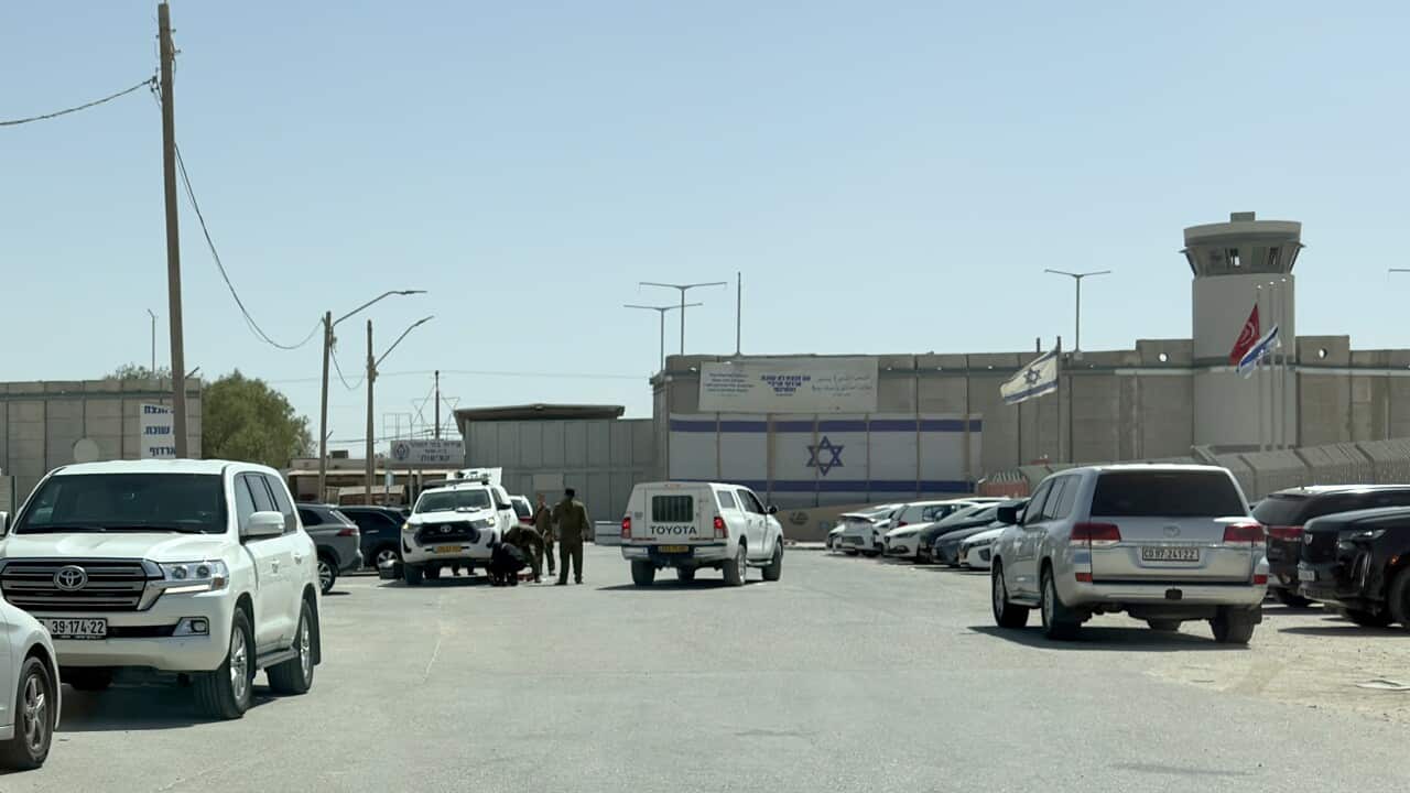 An Israeli prison facility is shown from the outside on a sunny day. Several white SUVs are parked in the foreground and a paved area leads toward the compound's walls, which are topped with a watchtower and display an Israeli flag and a sign in Hebrew and Arabic.
