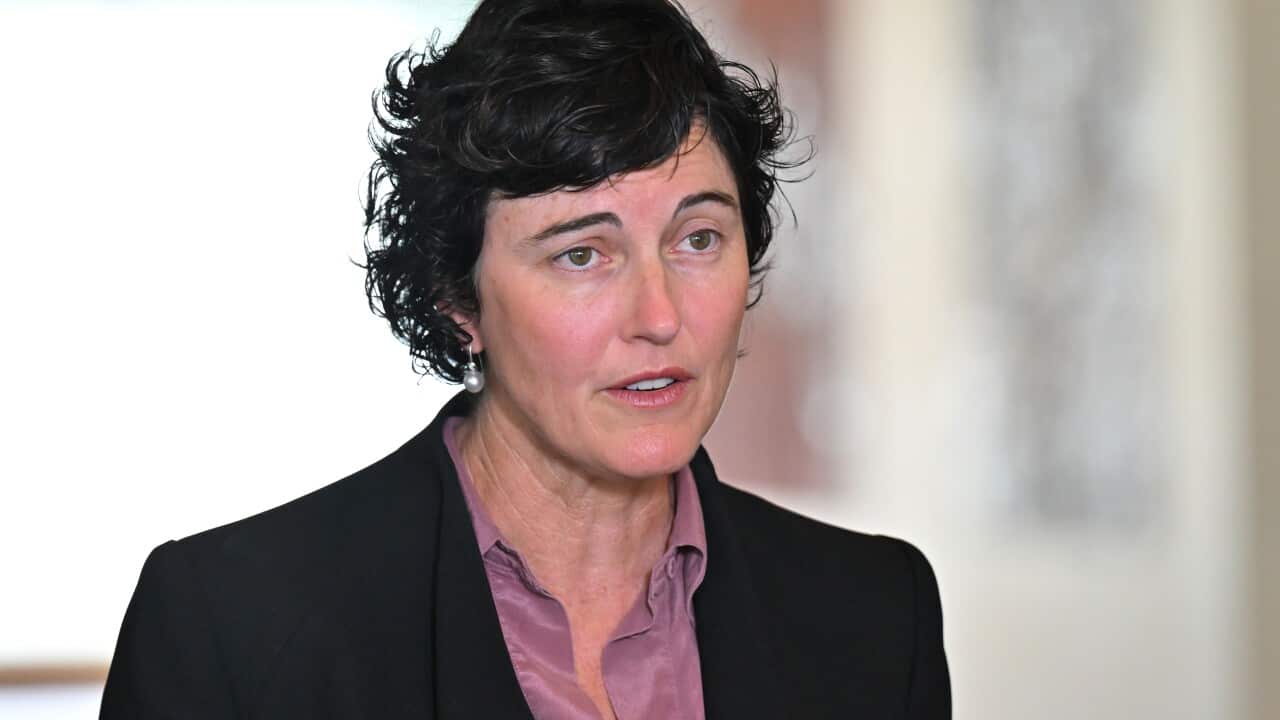 A woman in a black jacket and purple shirt, with short black hair.