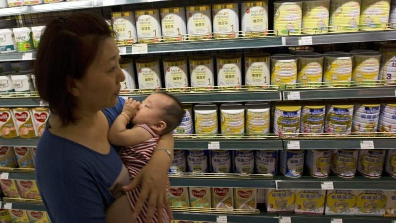 mum holding young baby passes shelves of infant formula in China shop