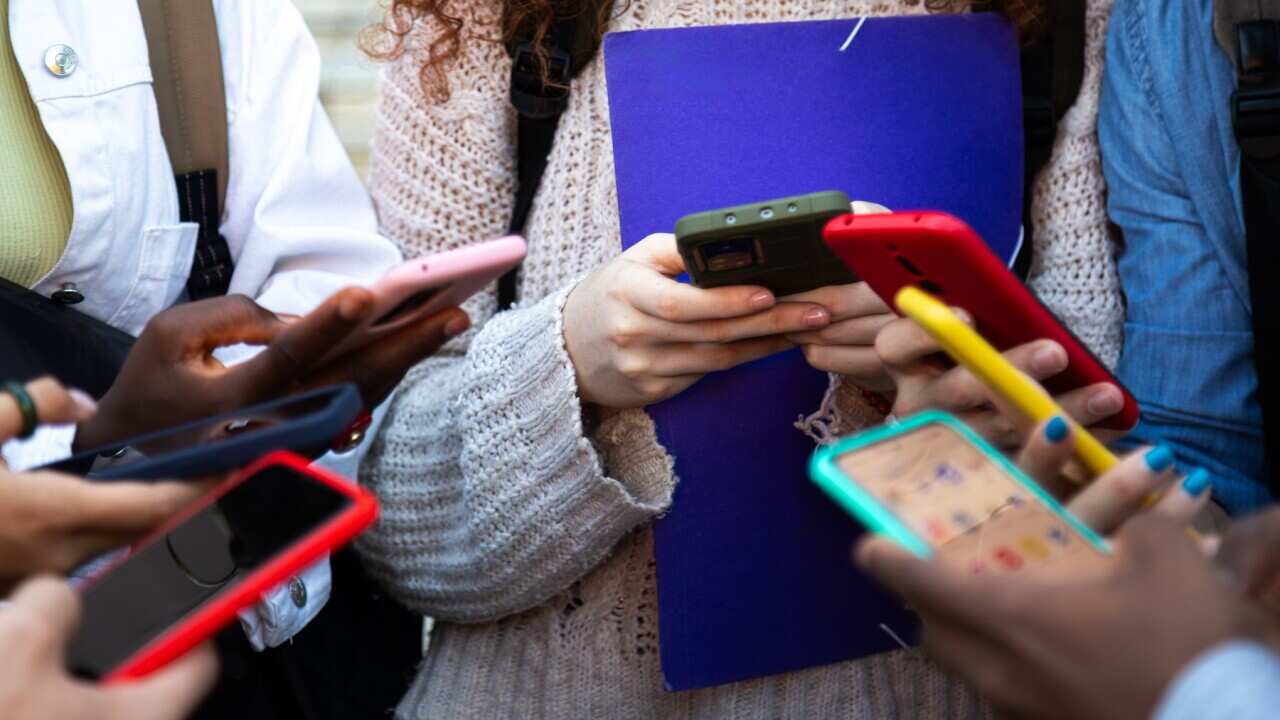 Close up of young college students hands holding mobile phones. Teenagers addicted to smartphones and technology. Group of friends sharing content on social media.