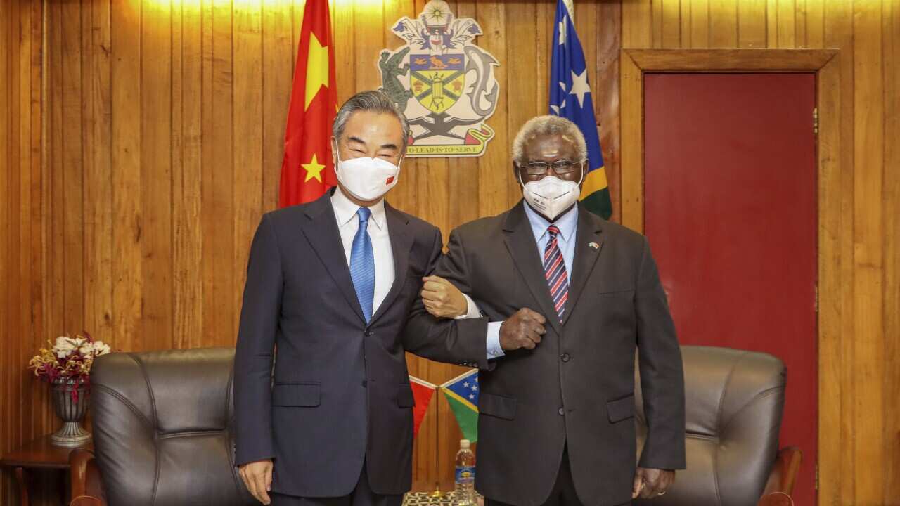 Solomon Islands Prime Minister Manasseh Sogavare at right lock arms with visiting Chinese Foreign Minister Wang Yi