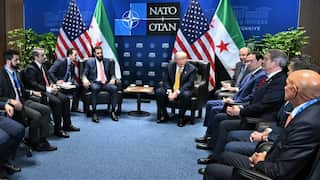Men in suits sit around in chairs facing Donald Trump in front of a NATO background.