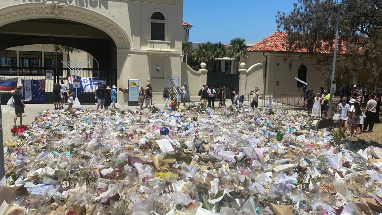 Floral tributes in front of a building with a sign on it reading Bondi Pavilion.