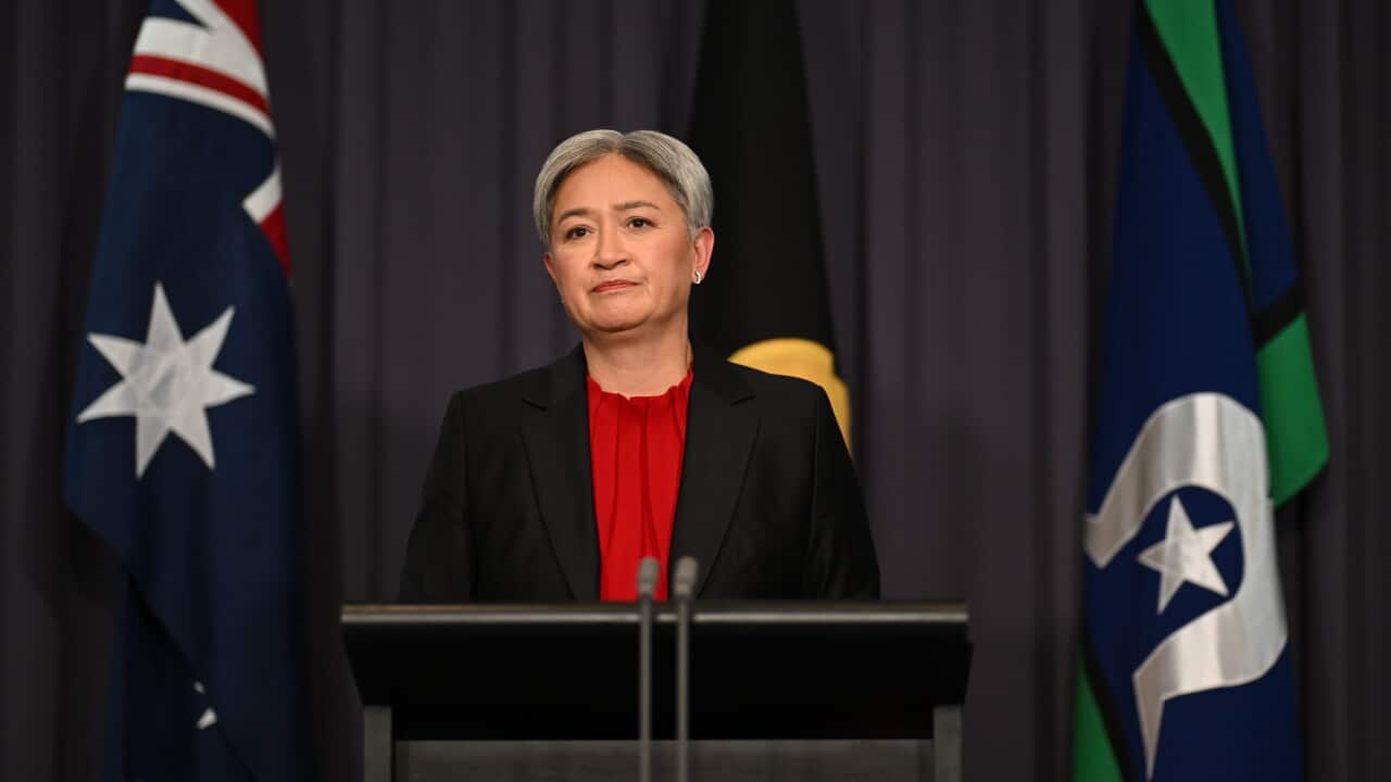 Australian Foreign Minister Penny Wong speaks at a press conference, standing behind a lectern with Australian and Aboriginal flags in the background.