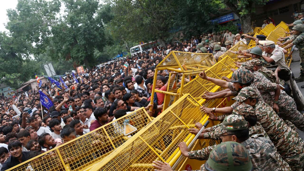 A crowd try to push through yellow barricades with police personnel trying to push from the opposite side