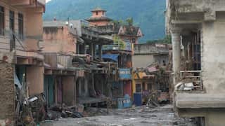 Flood-damaged street in Nepal, with mud and debris covering the road and several buildings heavily damaged by floodwaters.