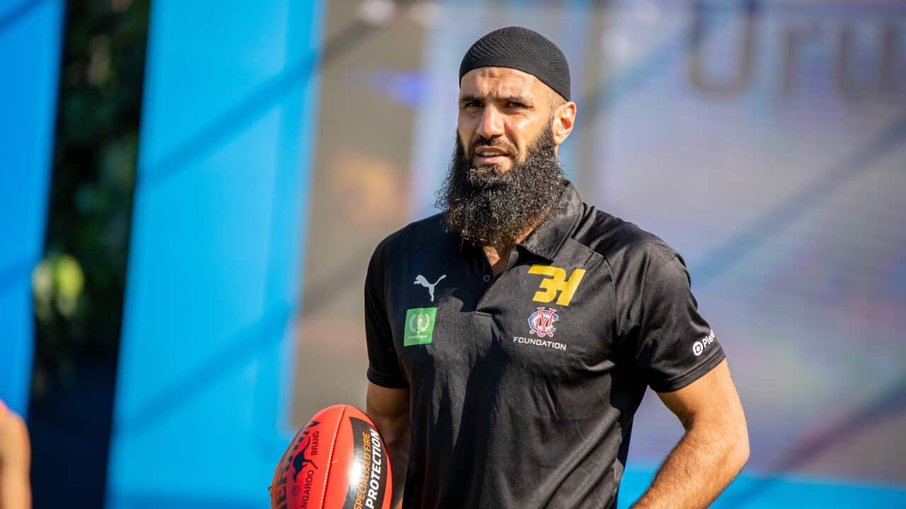 Bachar Houli is carrying an AFL football in his right hand wearing a black polo shirt and a black kufi.