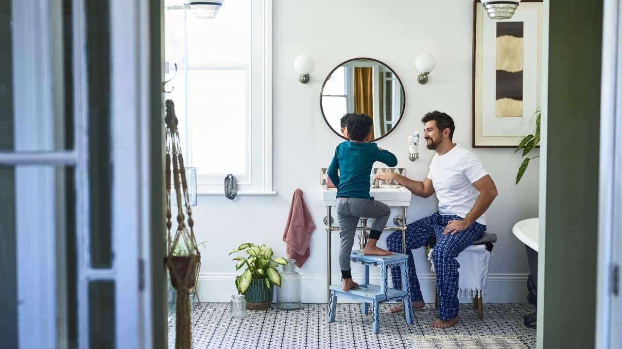 Father helping son brushing teeth in bathroom