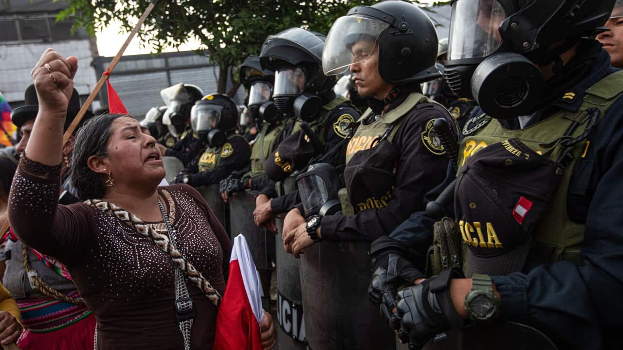 A woman yells in front of riot police officers.