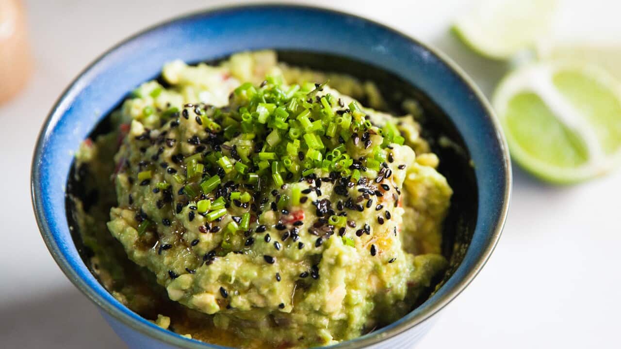 A deep blue pottery bowl holds a chunky acovado dip, topped with chopped chives. Lime wedges can be seen sitting behind the bowl, to one side.