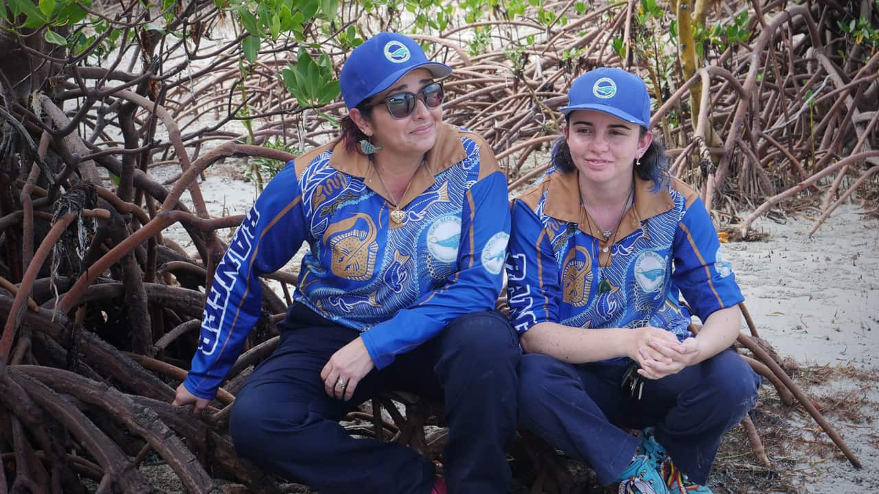 Two women from the Queensland Indigenous Women Rangers Network sitting on beach.