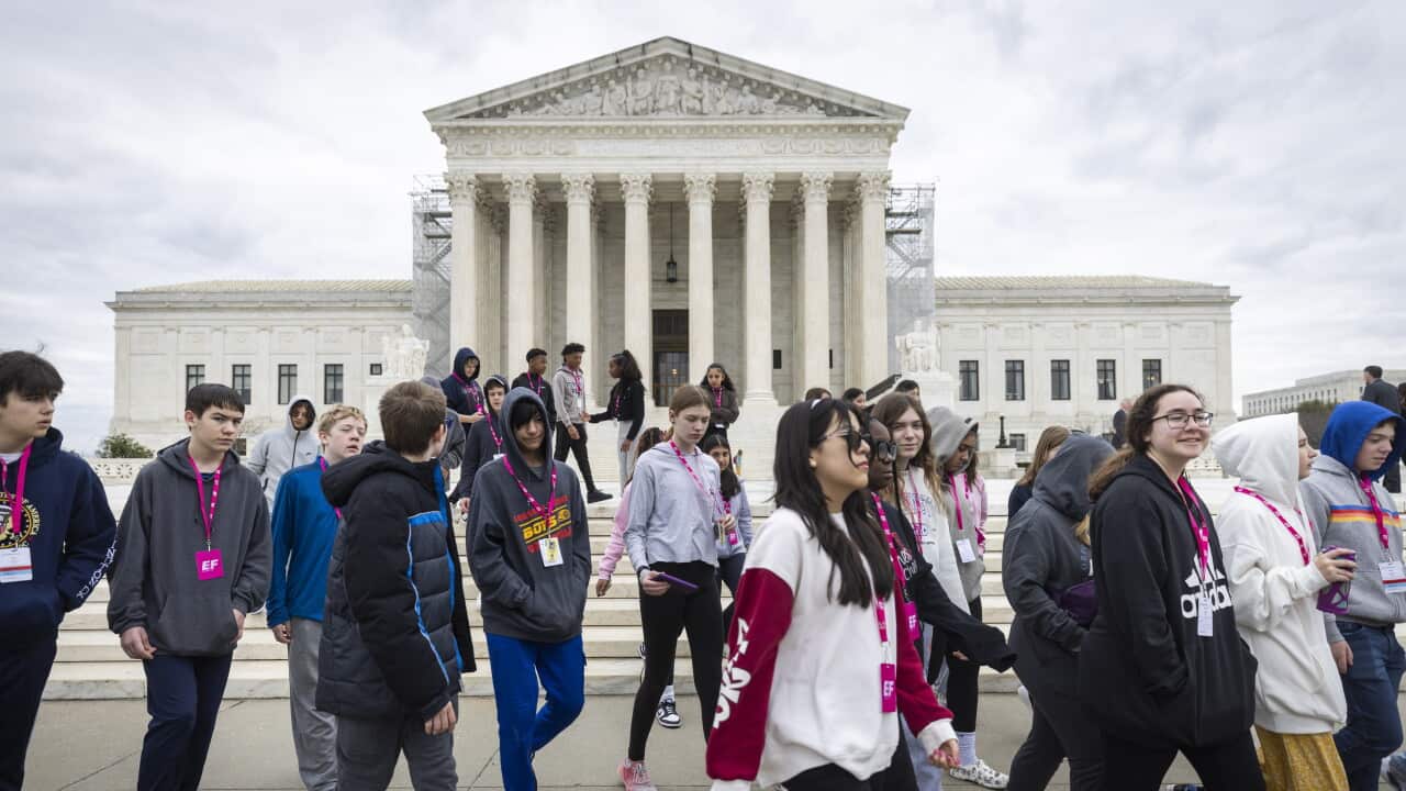 Group of students with lanyards around their necks walk past large, white US Supreme Court building.