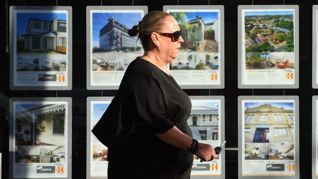 A woman walking past a window of real estate listings.