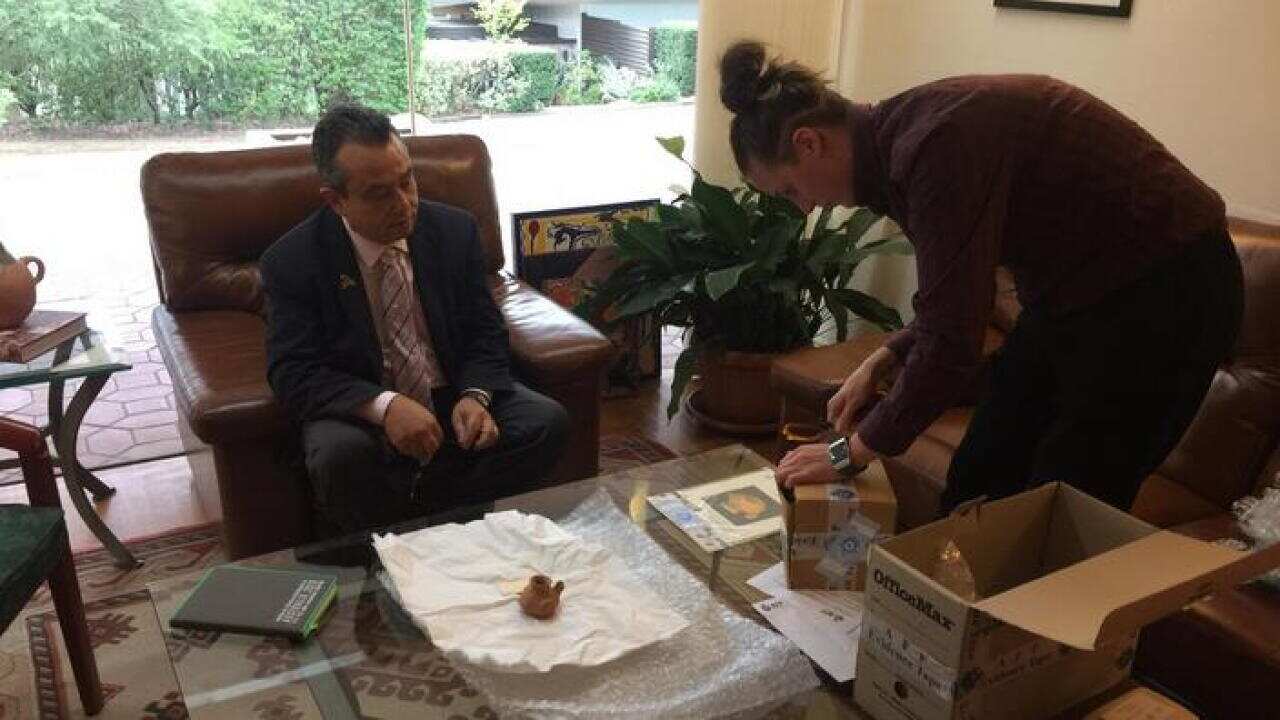 El embajador de México en Australia, Eduardo Peña Haller, al momento de recibir las piezas de manos de una agente de la Policía Federal de Australia.