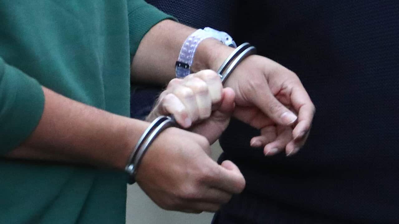A prisoner is led by handcuffs