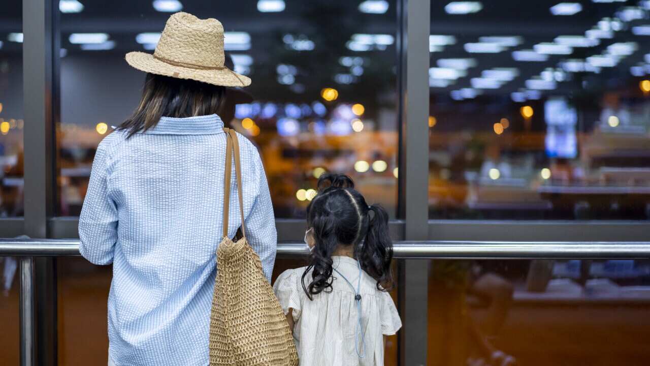 Mother and daughter looking outside through the transparent glass while waiting at the airport terminal early in the morning