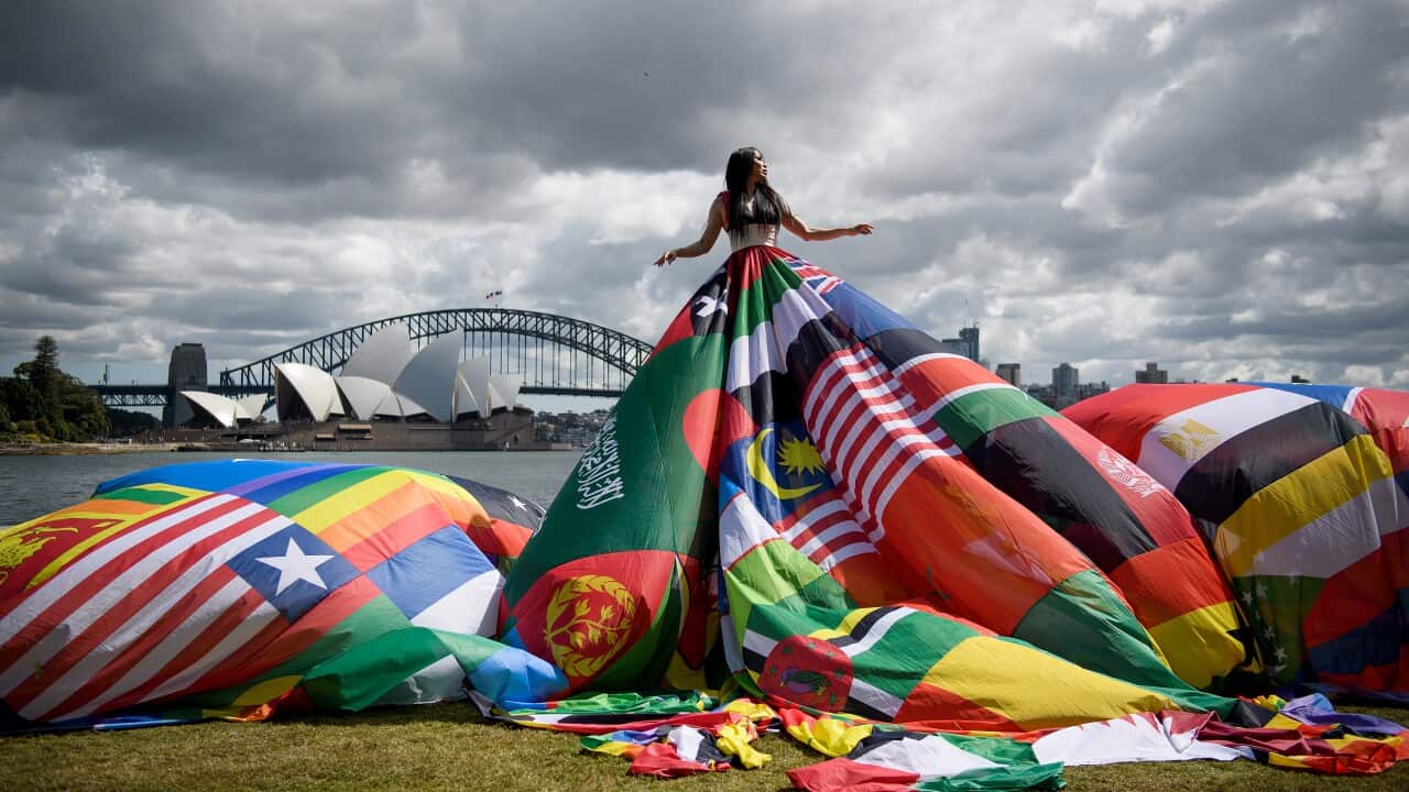 A woman stands in front of the Syndey Harbour Bridge wearing a dress made out of flags