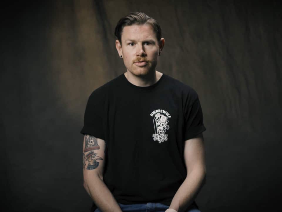 A man in a black t-shirt with tattoos sitting.
