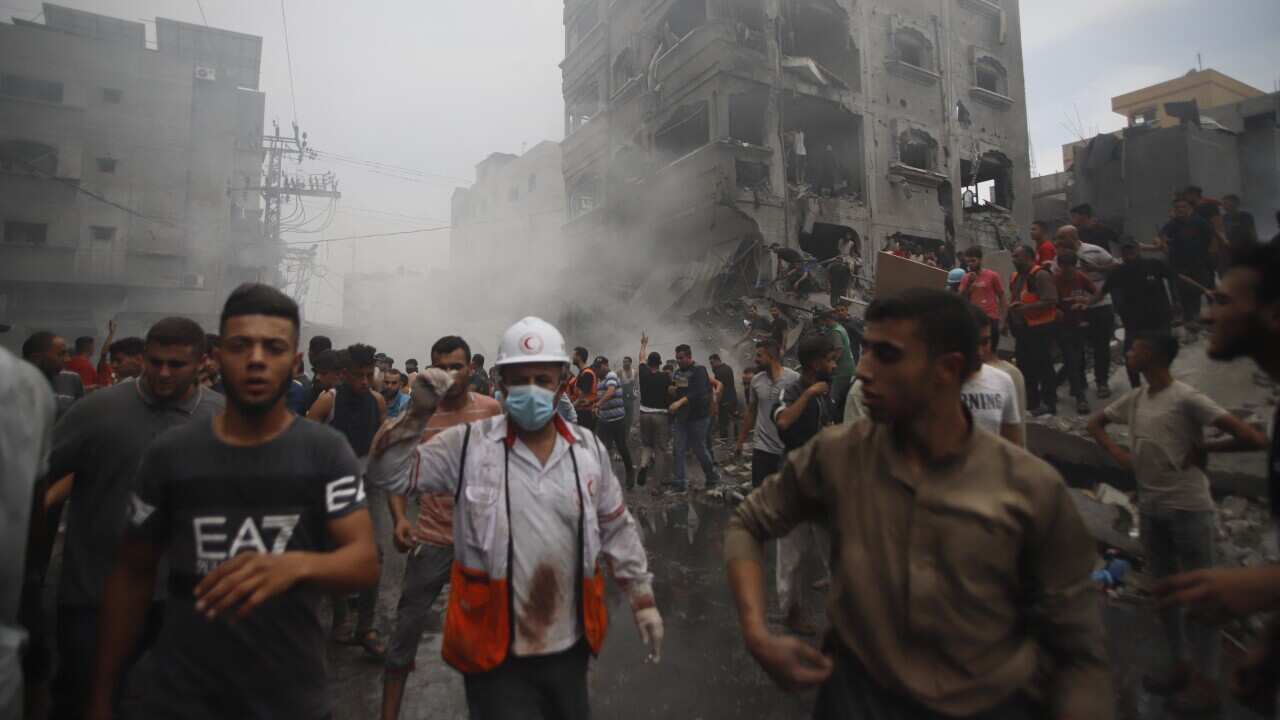 Crowds of people walking on the street. Behind them are destroyed buildings.
