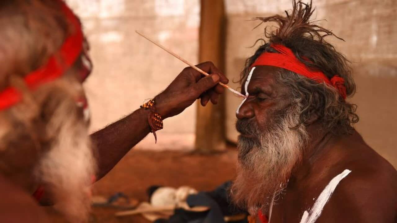 An Aboriginal elder paints a fellow elder before dancing at a cultural event near Uluru