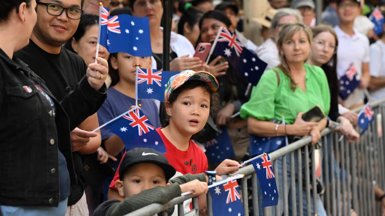 A close-up of children behind a barricade waving the Australian flag in a large crowd.