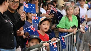 A close-up of children behind a barricade waving the Australian flag in a large crowd.