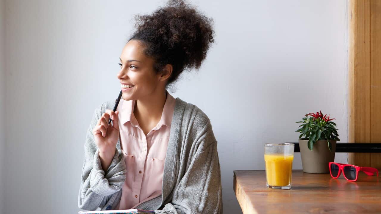 Happy young woman sitting at home with pen and paper