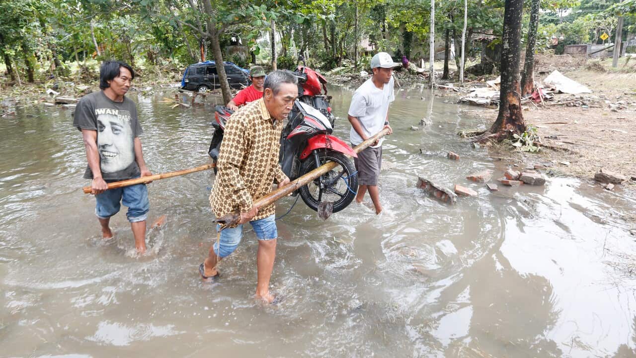 Local residents carry a scooter among debris in a devastated area after a tsunami hit Sunda Strait in Carita, Banten, Indonesia.