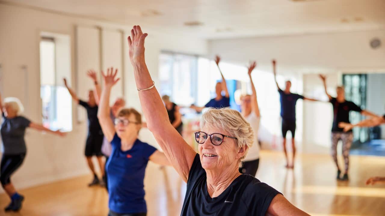 Smiling senior woman and others taking an exercise class at the gym