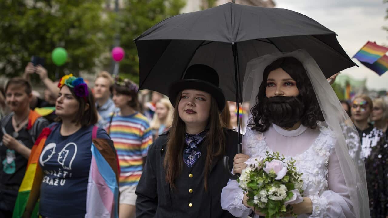 A woman dressed in a top hat and suit and another wearing a wedding dress, veil, and beard participate in the Baltic Pride Parade in Vilnius, Lithuania