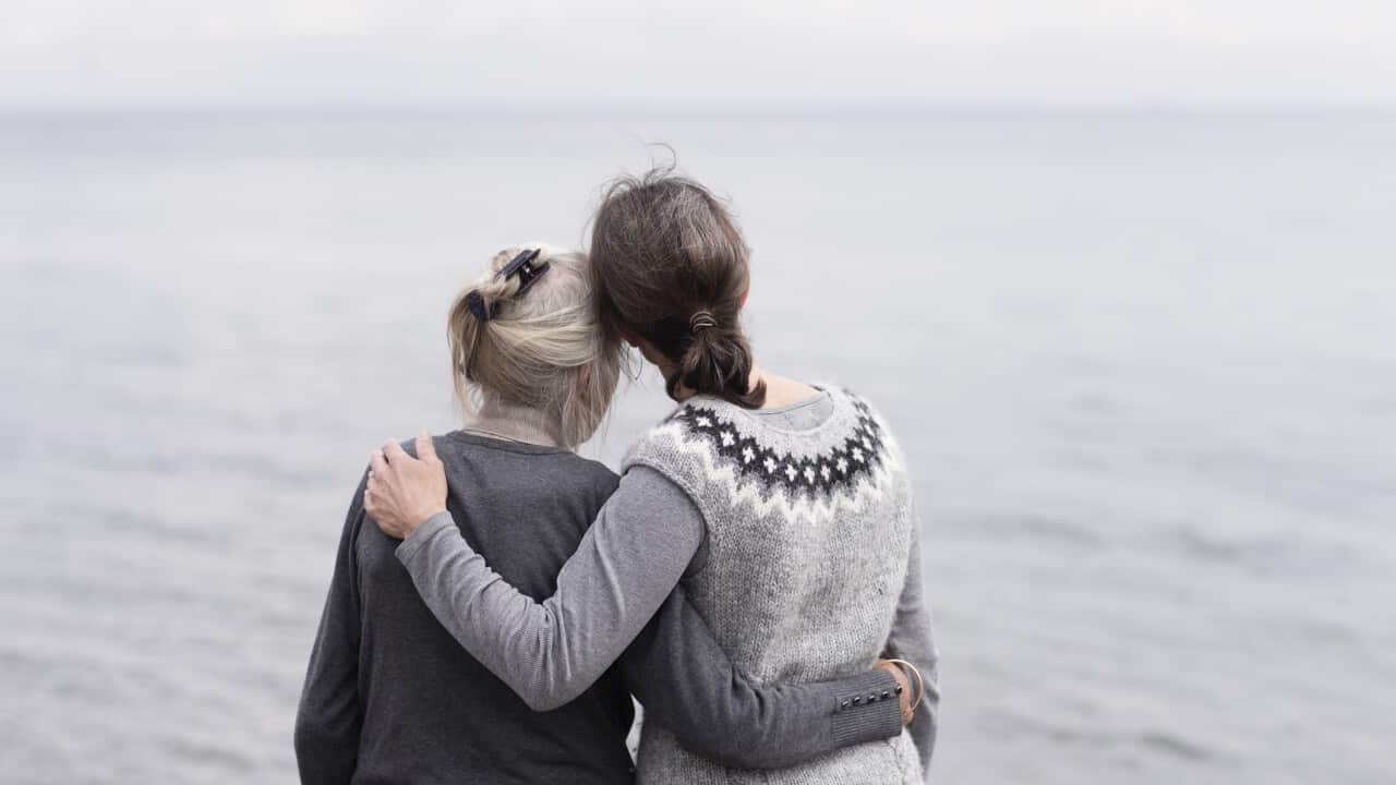 two generations women embracing, looking at sea
