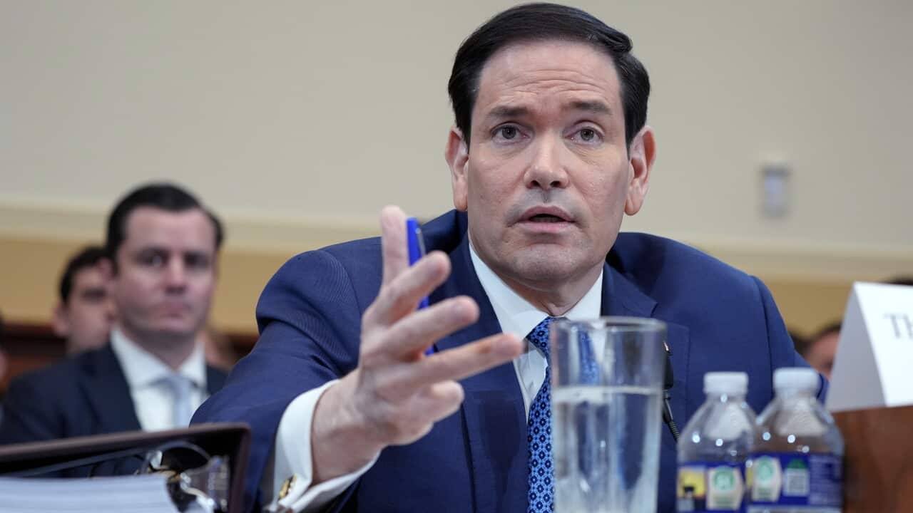 Marco Rubio, a middle aged man with black hair in blue suit and tie, speaks into a microphone.