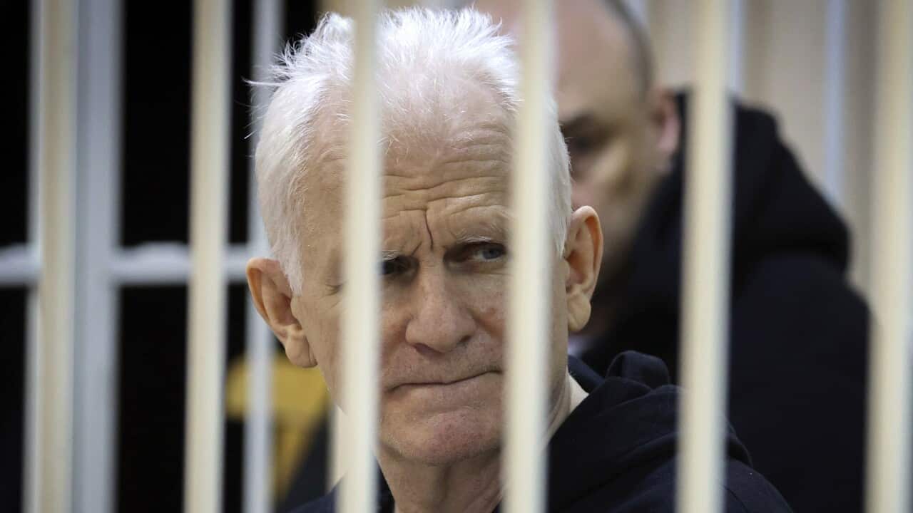 A man with white hair wearing a black hoodie is seen behind white bars