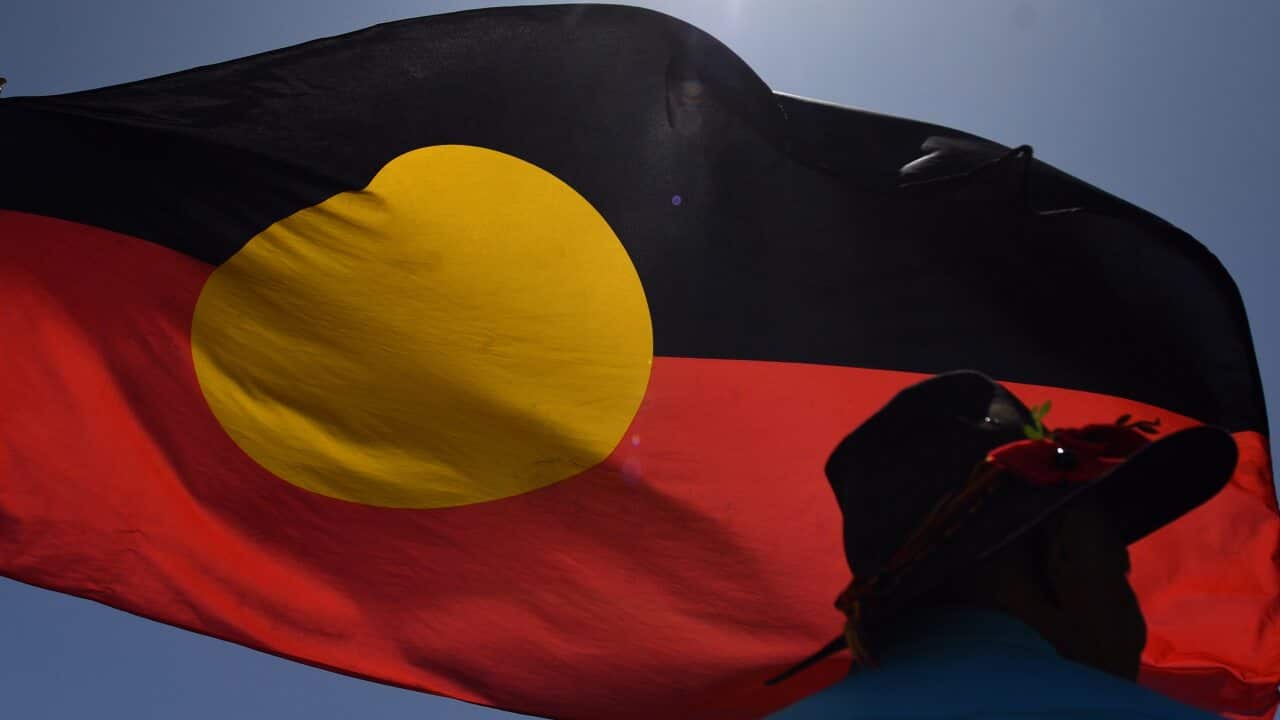 A man is seen under the indigenous flag protesting Aboriginal rights on Australia Day at Parliament House in Canberra, Sunday, January 26, 2020. (AAP Image/Mick Tsikas) NO ARCHIVING