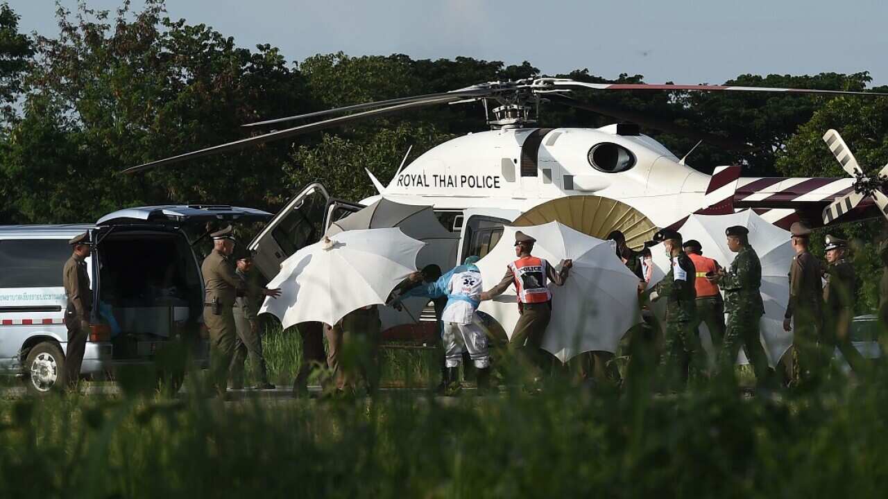 Police and military personnel use umbrellas to cover around a stretcher near a helicopter and an ambulance at a military airport in Chiang Rai.