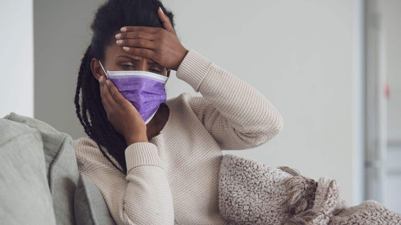 Woman with hand on forehead,checking fever, lying on the couch covered with a blanket.The woman using a face mask to prevent other people from getting infected