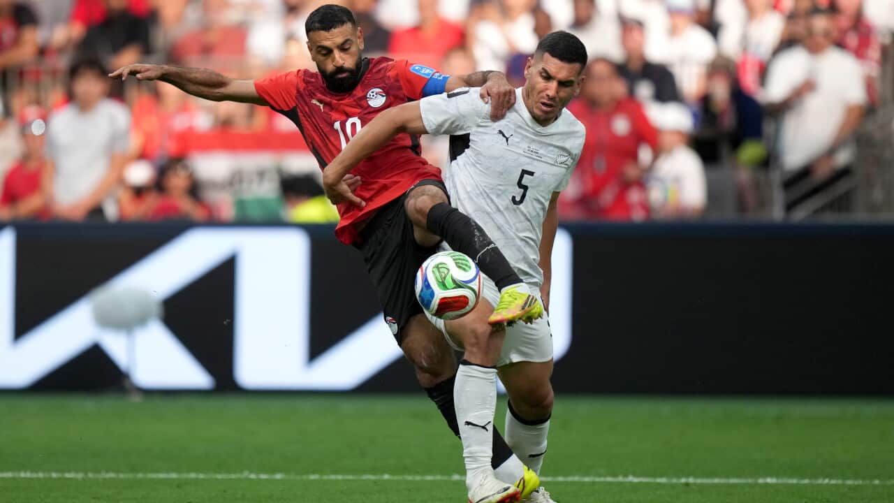 Two footballers, one in a red jersey and one in white, tussle over a football during a match.