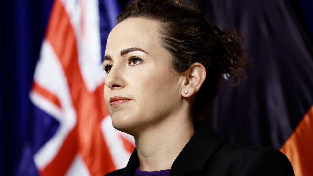 A woman staring ahead. An Australian flag is behind her.