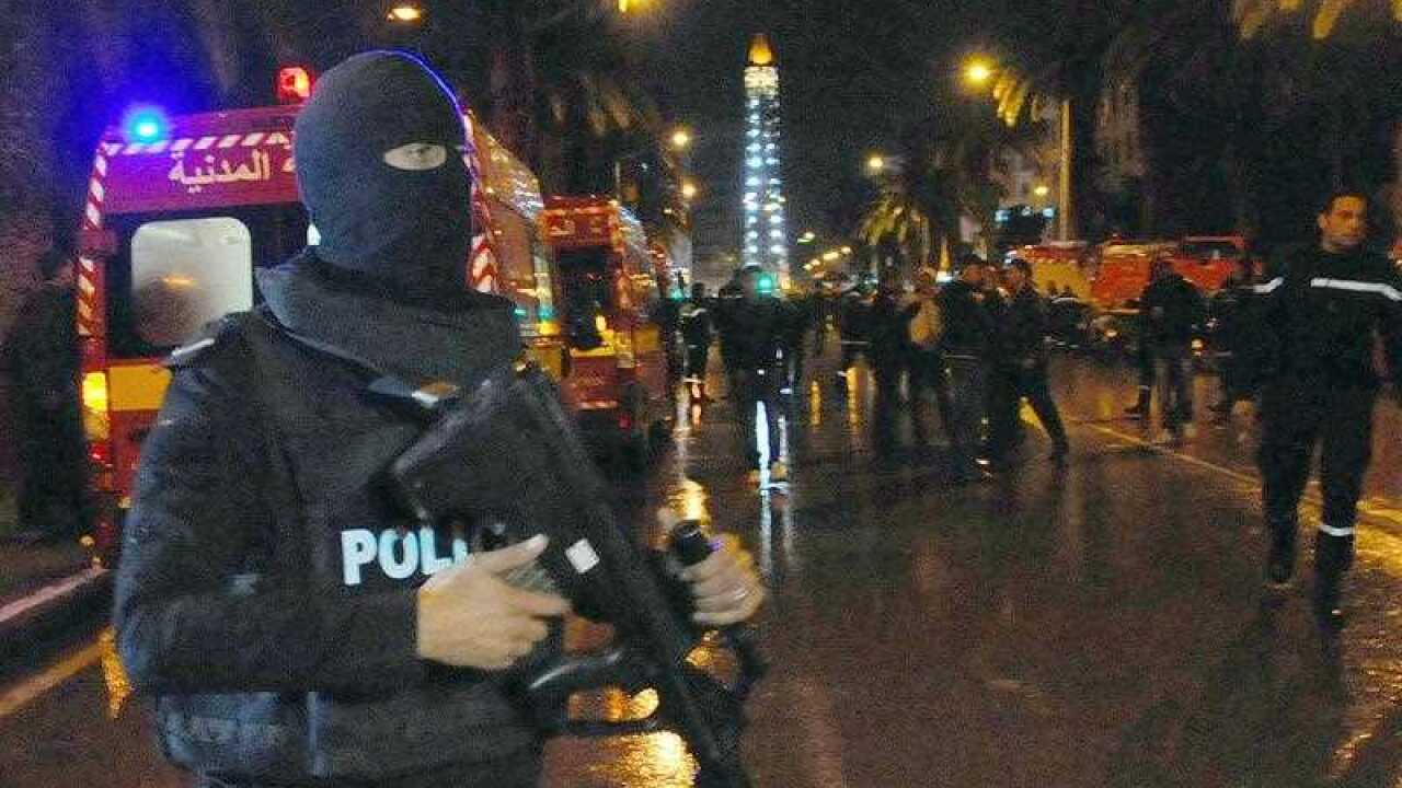 A hooded police officer prevents media from aproaching the scene of a bus explosion in the center of the capital, Tunis, Tunisia, Tuesday, Nov. 24, 2015.