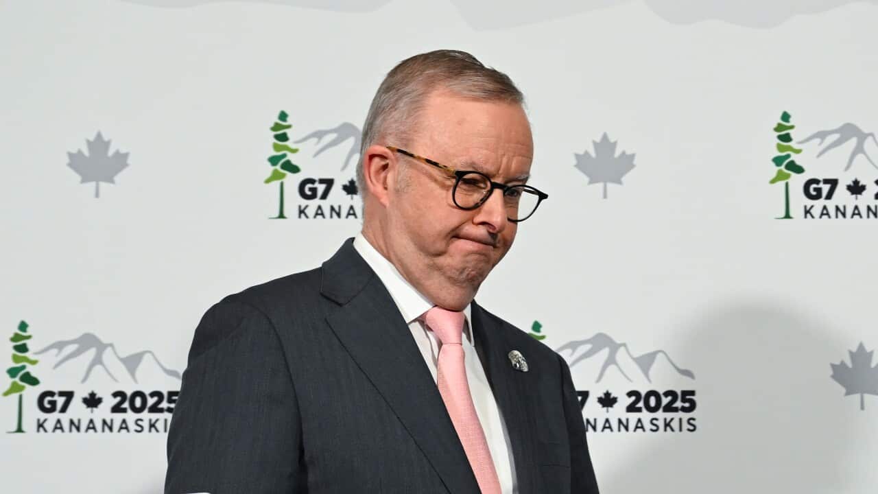 Prime Minister Anthony Albanese, wearing a suit, tie and glasses, leaving a press conference. Behind him is backdrop that says: G7 2025 Kanaskis.