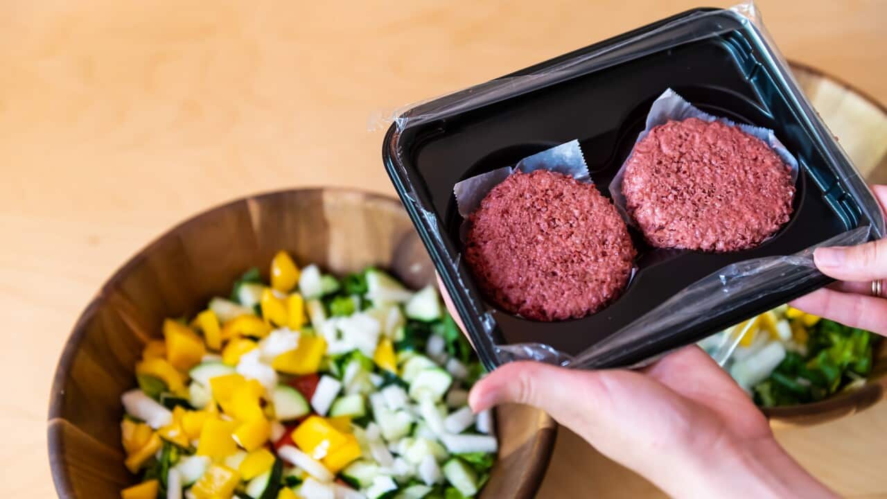 Woman holding two raw uncooked red vegan meat burger patties by salad bowls in packaging