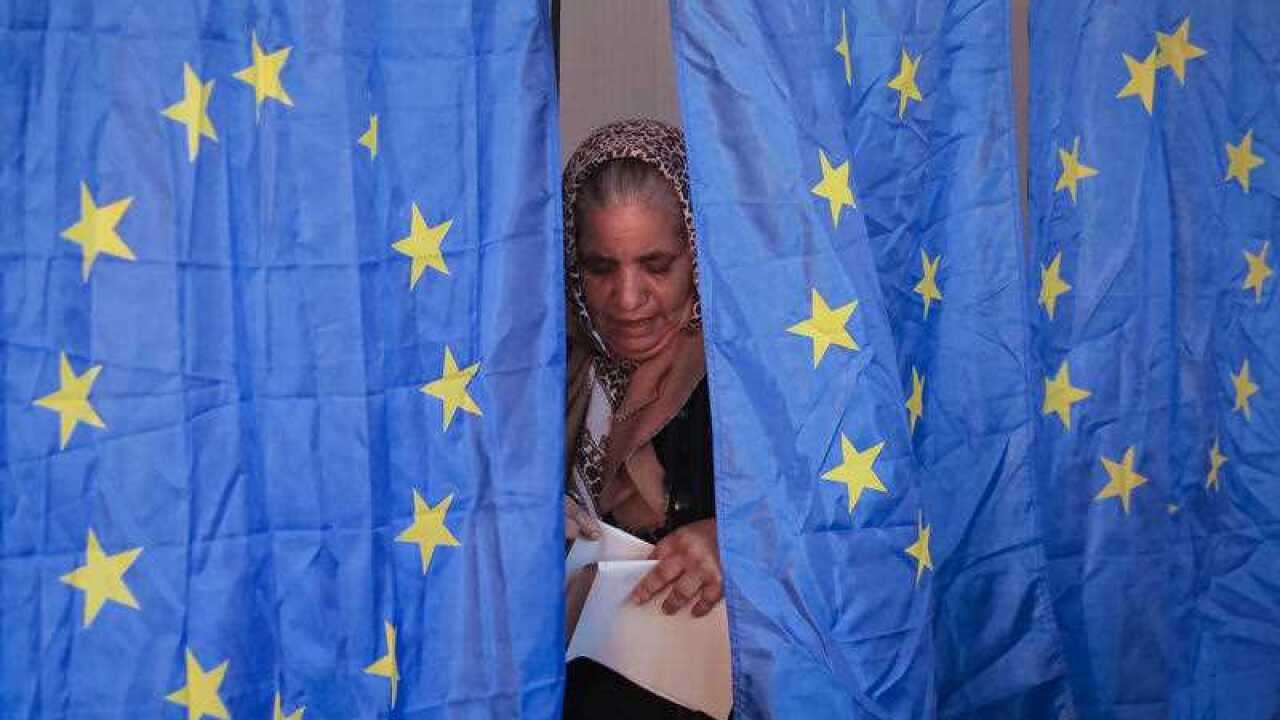 A woman exits a voting booth, with European Union flags as curtains, in Baleni Sarbi, Romania, Sunday, Dec. 11, 2016.