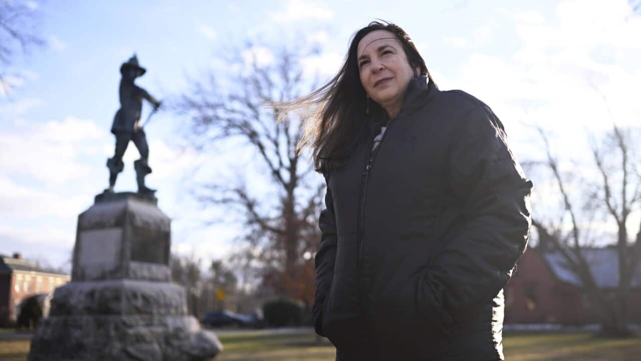 A woman stands in front of a statue of a man with a sword behind her.