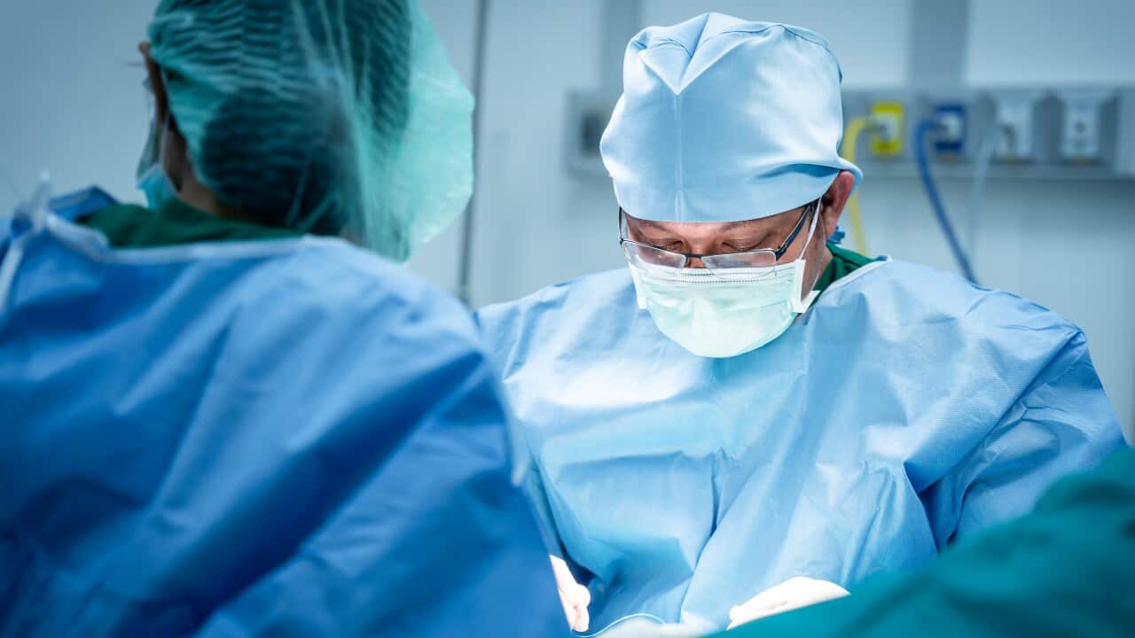 A surgeon in blue scrubs operates on a person