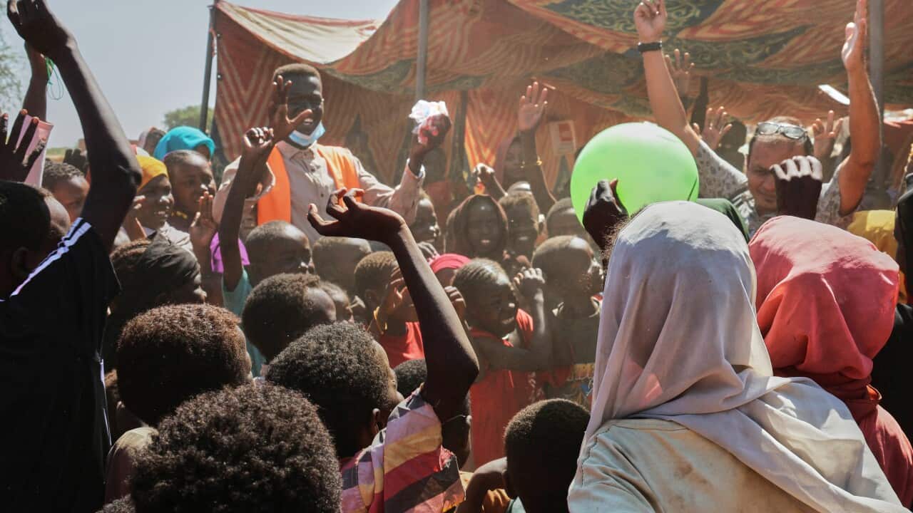 A crowd of people, including many children, in an area with tents.