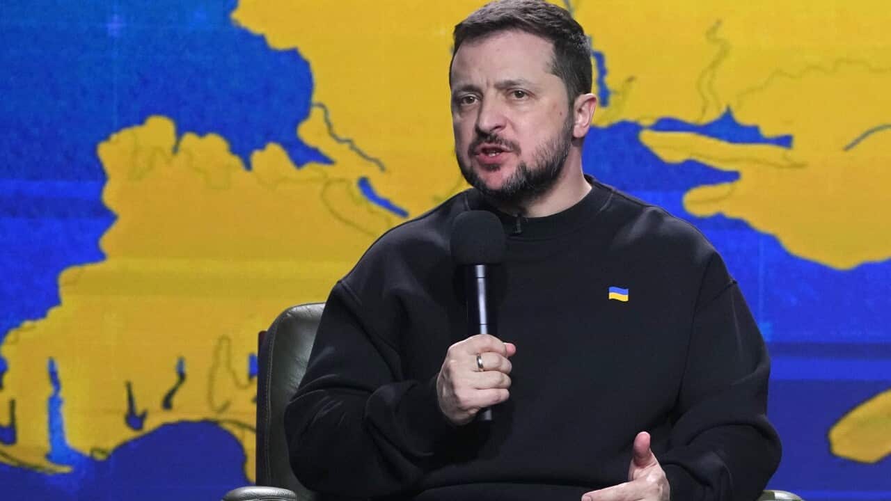 Ukrainian President Volodymyr Zelenskyy holds a microphone while seated.