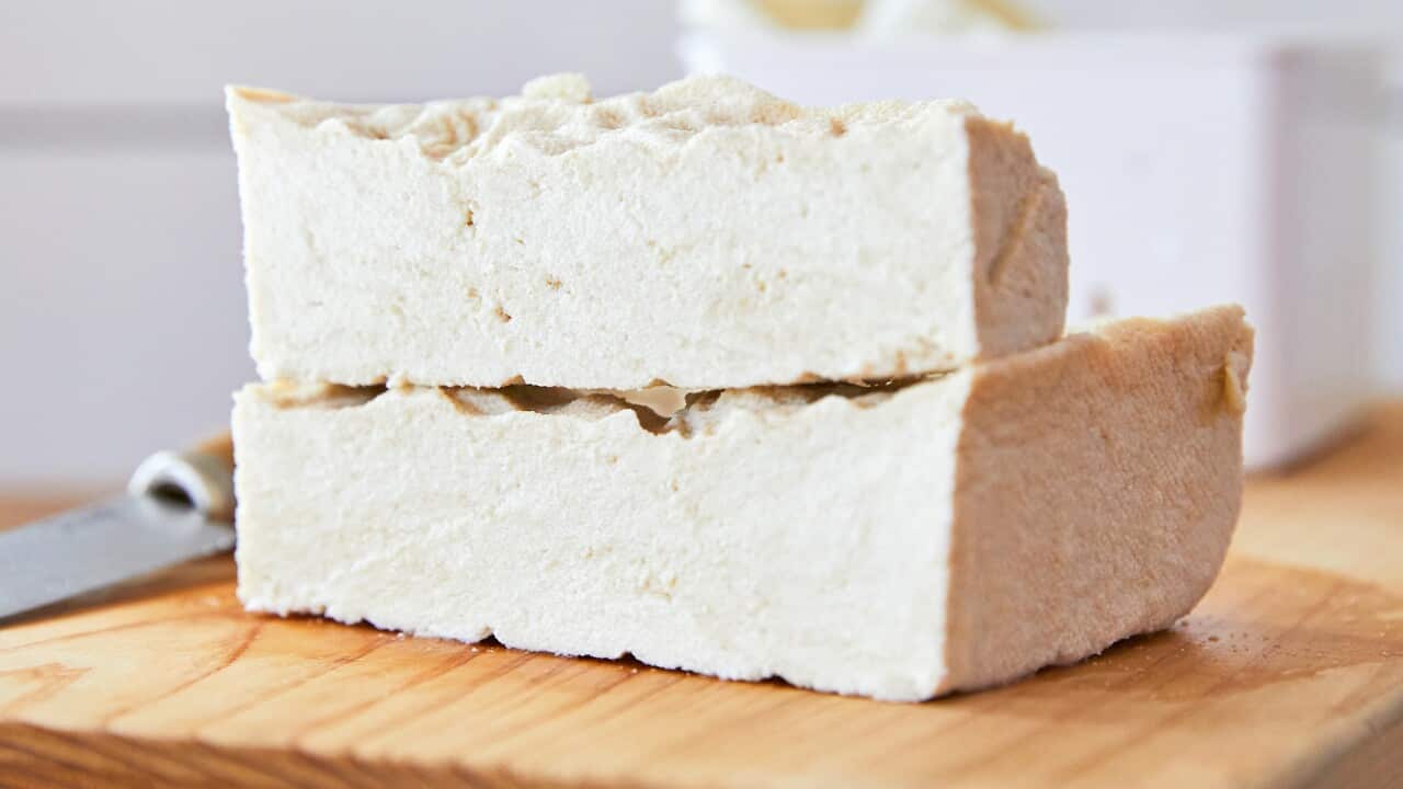 Two blocks of tofu are stacked on a wooden board.